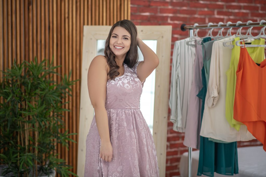 Young plus-size woman in a pink dress standing in a clothes store
