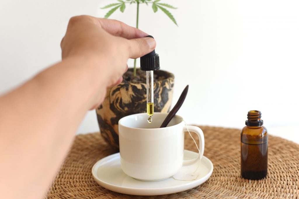 Hand pouring drops of hemp oil in breakfast infusion